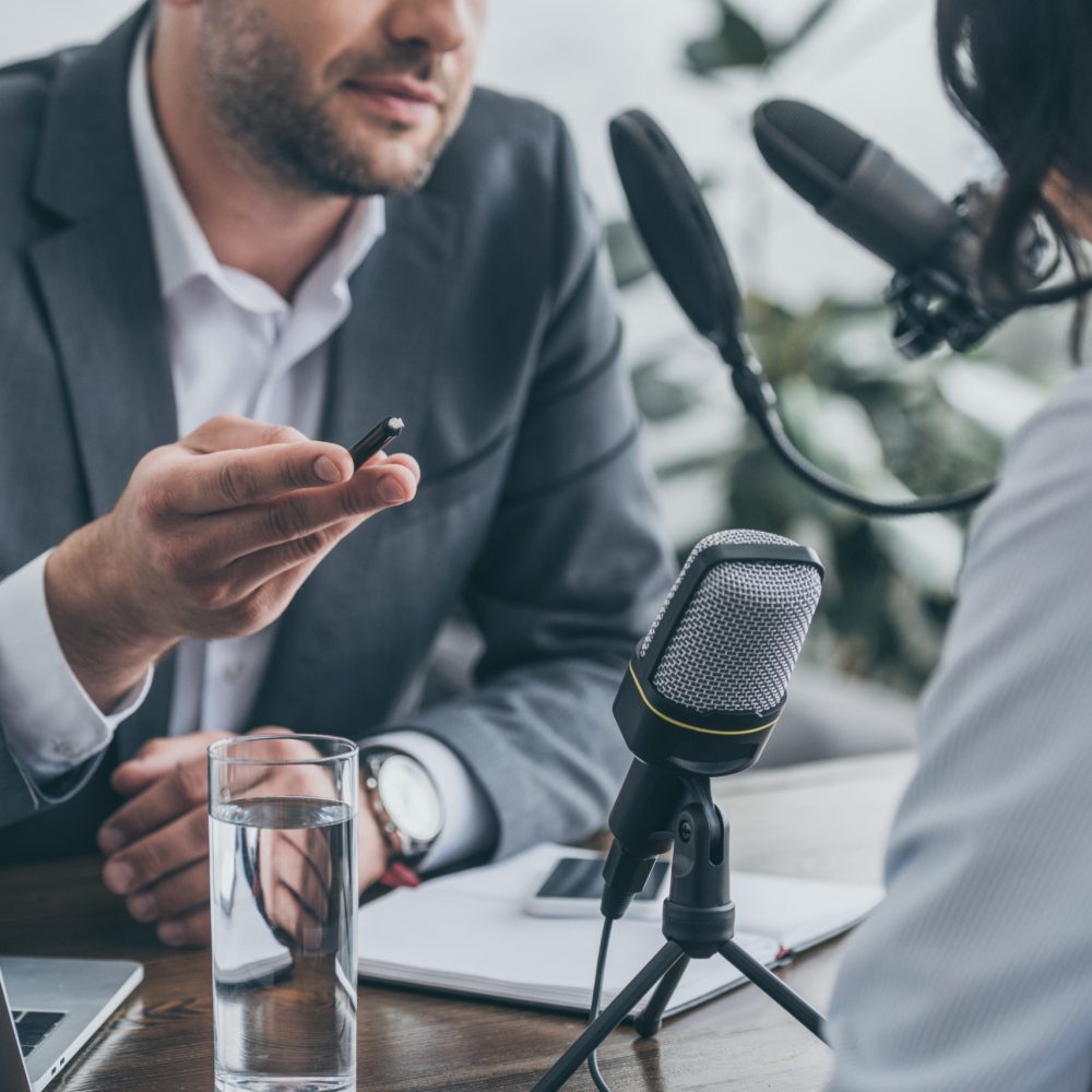 cropped view of radio host gesturing while interviewing businesswoman in broadcasting studio